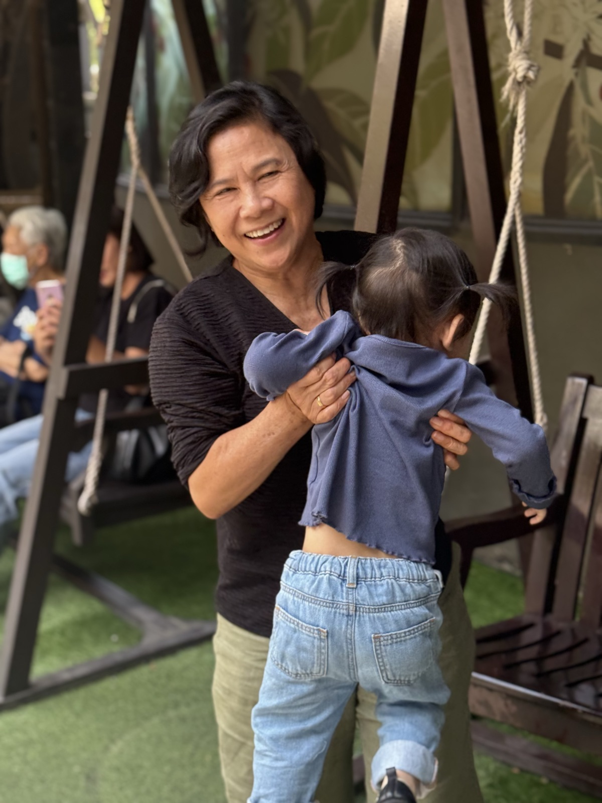 Mommy Moo laughing while lifting her granddaughter onto a garden swing